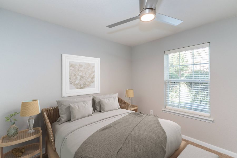 Attain on 5th apartment homes with A cozy bedroom with a made bed, two lamps, a window, and a ceiling fan.