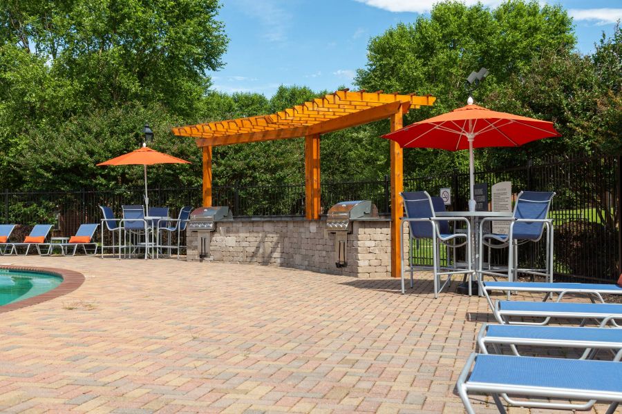 Attain on 5th apartment homes with Outdoor grilling area with pergola, lounge chairs, red umbrellas, and pool on a sunny day.