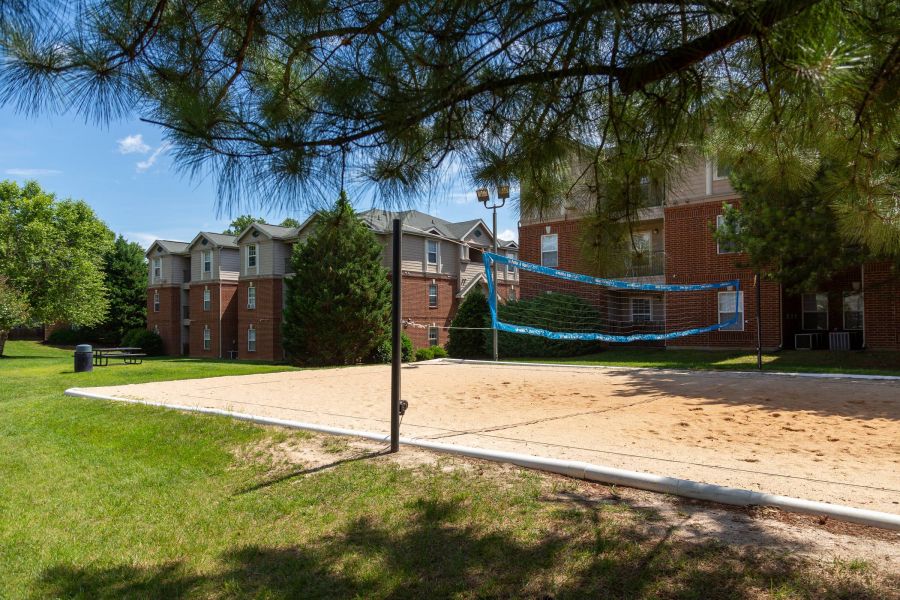 Attain on 5th apartment homes with Sandy volleyball court outside brick apartment buildings surrounded by green grass and trees.