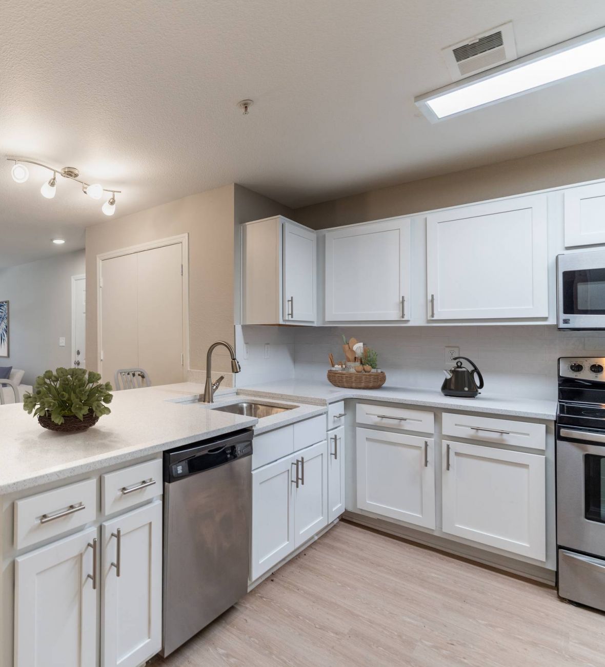 Attain on 5th apartment homes with Modern open-plan kitchen with white cabinets, island, and view of living room with sofa and TV.