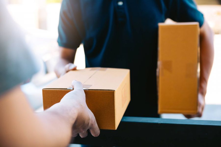 Attain on 5th apartment homes with Person handing a cardboard box to another person holding a package, likely during a delivery.