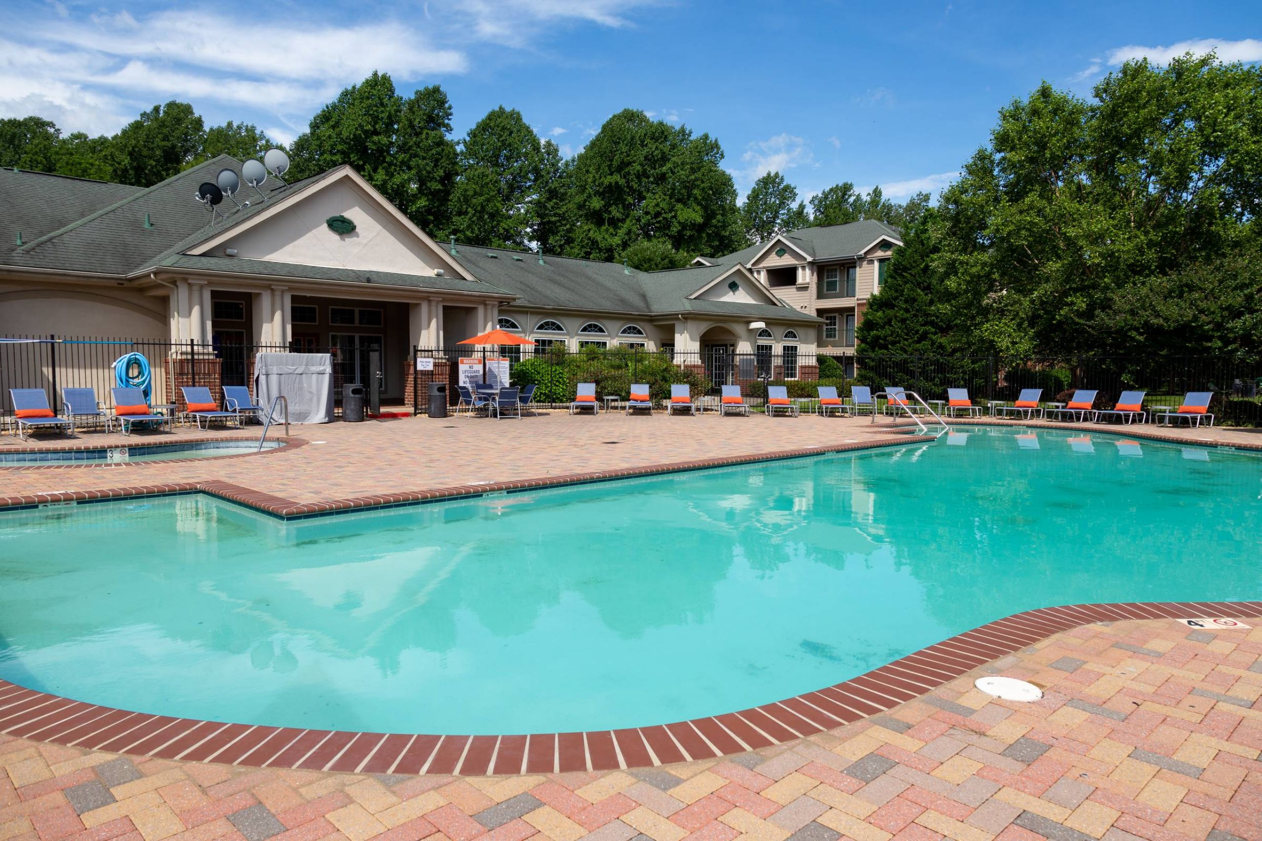 Attain on 5th apartment homes with Outdoor swimming pool with lounge chairs and a clubhouse building surrounded by trees on a sunny day.