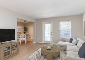 Attain on 5th apartment homes with Bright living room with a beige sofa, round wooden coffee table, TV, and adjacent dining area with a table and chairs.