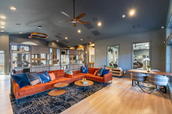 Attain on 5th apartment homes with Modern lounge with orange sofa, round tables, shelves, and large windows, featuring warm and neutral tones.