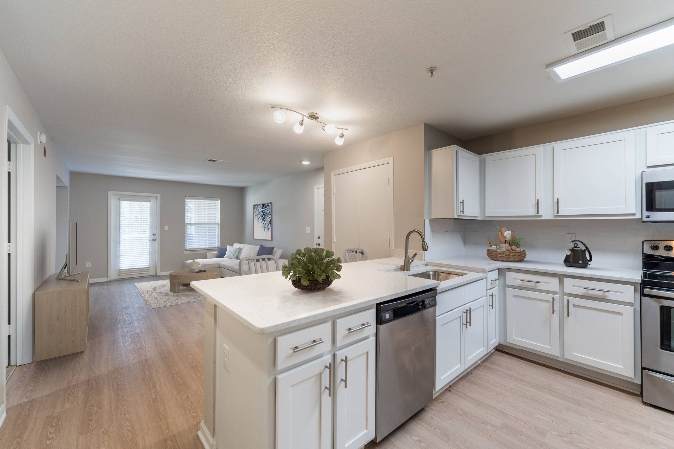 Attain on 5th apartment homes with Modern open-plan kitchen with white cabinets, island, and view of living room with sofa and TV.