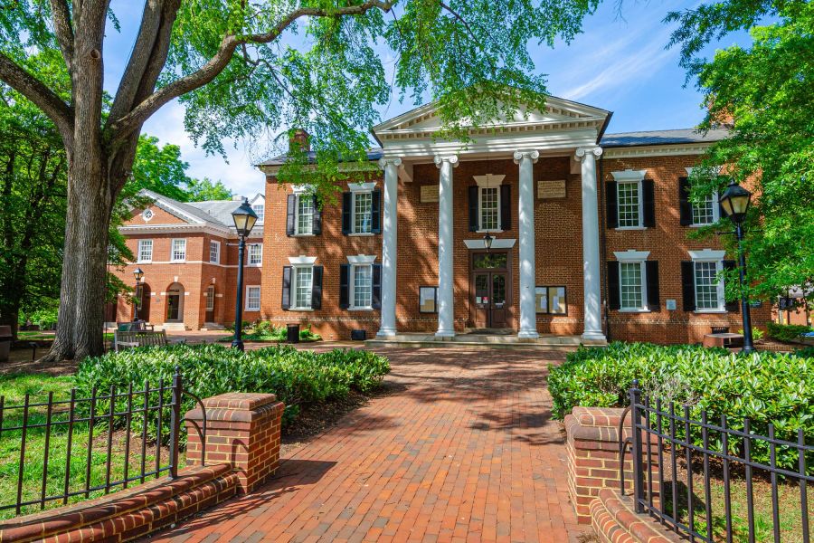 Attain on 5th apartment homes with Red-brick building with white columns and a brick walkway, surrounded by trees and greenery on a sunny day.