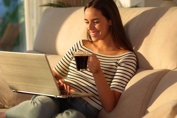 Attain on 5th apartment homes with Smiling woman sitting on a couch with a laptop and holding a cup of coffee in a sunlit room.