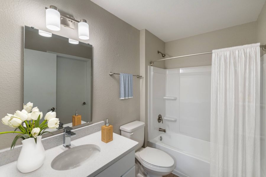 Attain on 5th apartment homes with Modern bathroom with a white sink, toilet, bathtub, shower curtain, and vase of white flowers on the counter.
