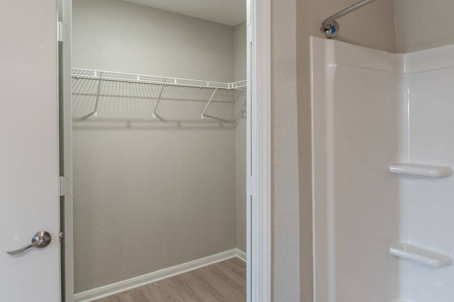 Attain on 5th apartment homes with Open door reveals an empty walk-in closet next to a white bathtub and shower in a bathroom.