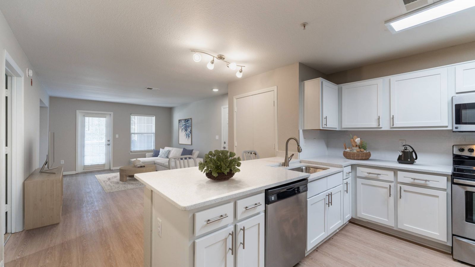 Modern kitchen and living area with white cabinets, stainless steel appliances, and a large island. Cozy seating area with a sofa and rug in the background. Bright and inviting atmosphere.