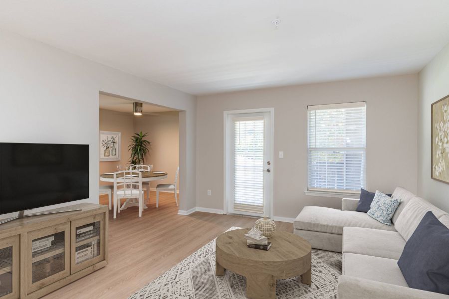 Attain on 5th apartment homes with Bright living room with a beige sofa, TV, round coffee table, and view into a dining area with a table and chairs.