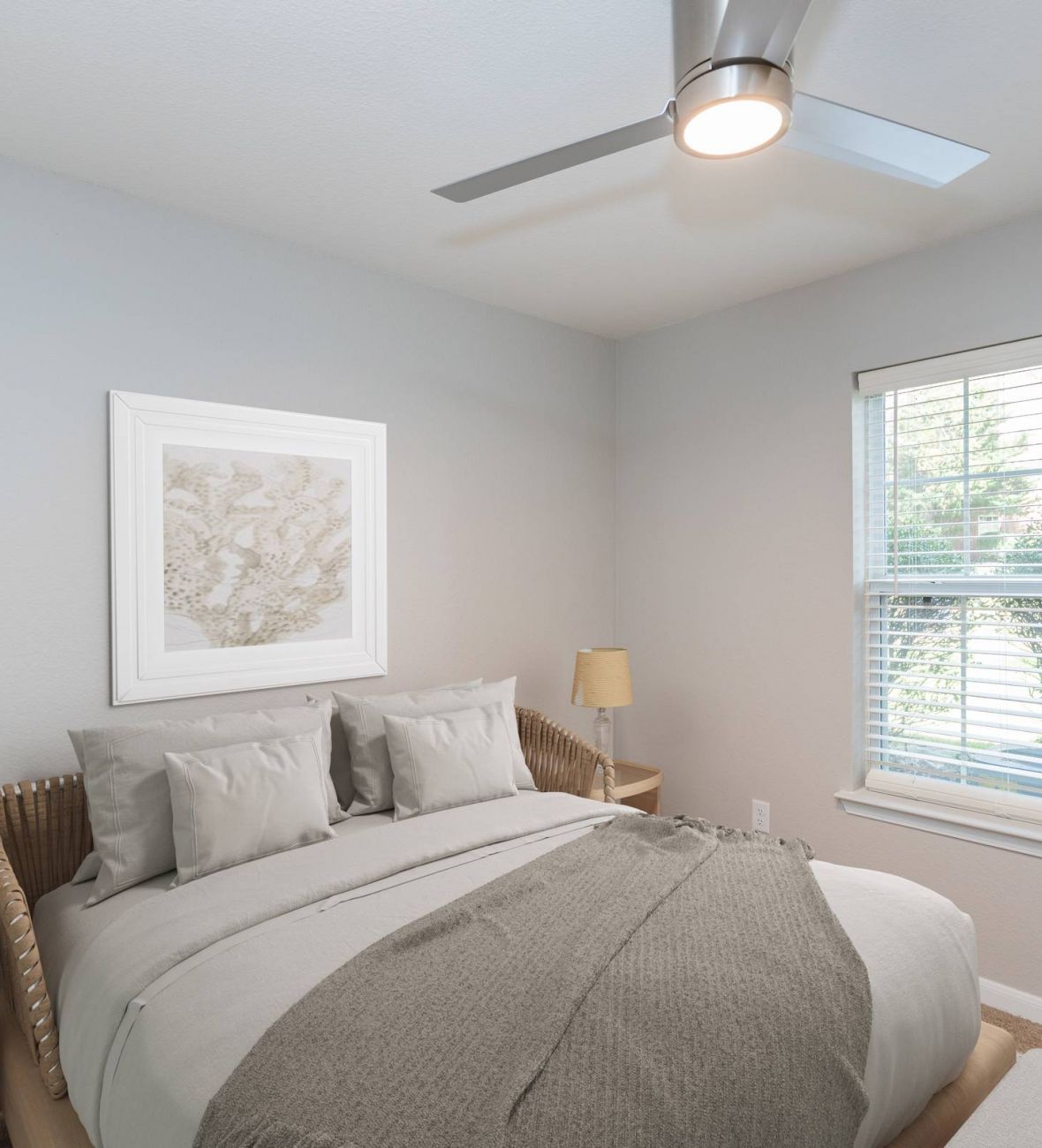 Attain on 5th apartment homes with A cozy bedroom with a made bed, two lamps, a window, and a ceiling fan.