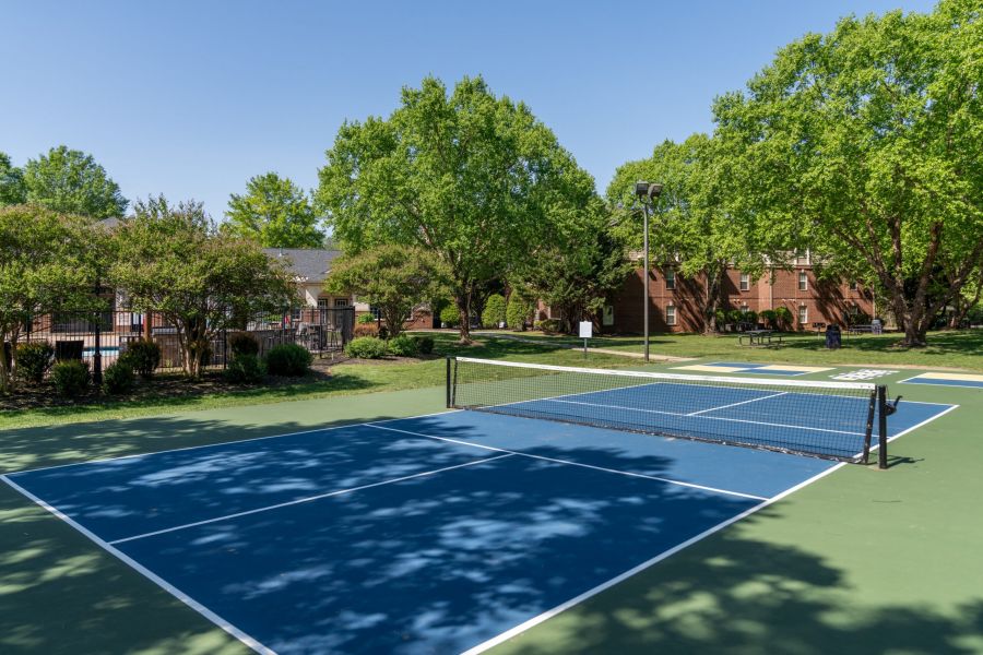 Attain on 5th apartment homes with Blue and green outdoor tennis court surrounded by trees and brick buildings on a sunny day.