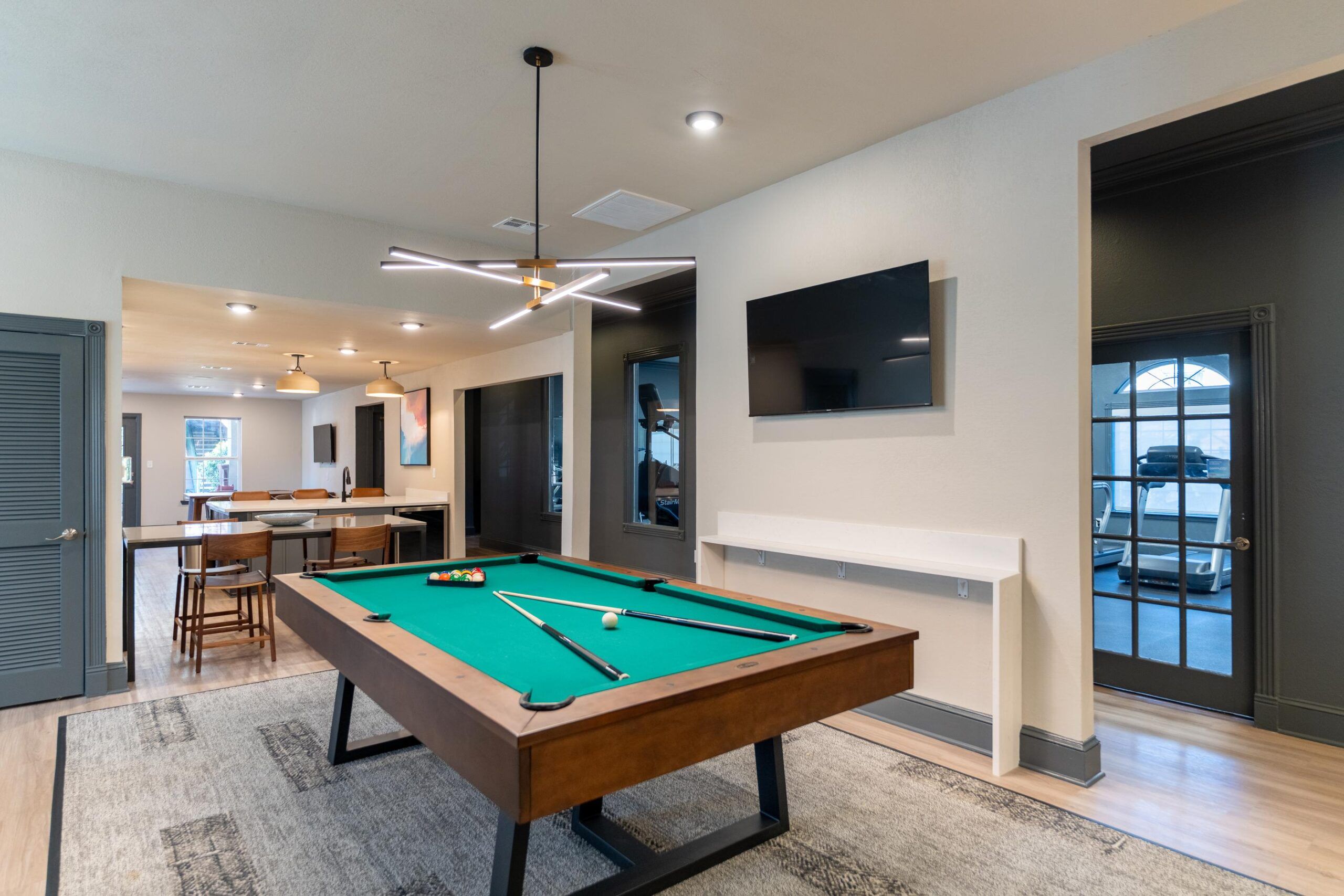 Attain on 5th apartment homes with Modern game room with a pool table, wall-mounted TV, bar seating, and stylish lighting fixtures.